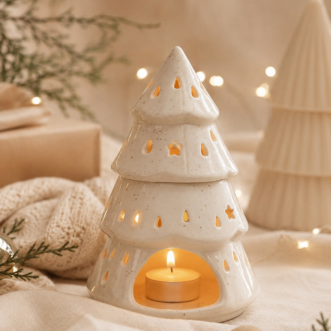 Quemador de cera aromática en forma de árbol de Navidad con vela de té encendida en su interior, sobre decoración navideña.