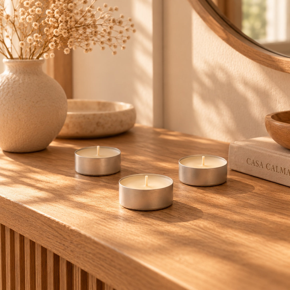 Tres velas de té blancas de regalo sobre un mueble de madera junto a un espejo, para quemador de wax melts