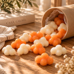 Wax melts de mandarina y champán de Casa Calma en forma de nubes blancas y naranjas, saliendo de un envase de cartón tumbado.