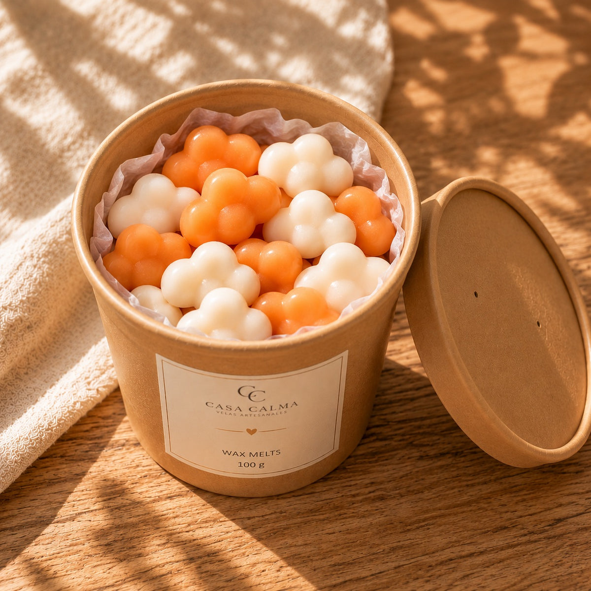 Envase abierto de wax melts de mandarina y champán de Casa Calma, con nubes blancas y naranjas y la tapa a un lado.