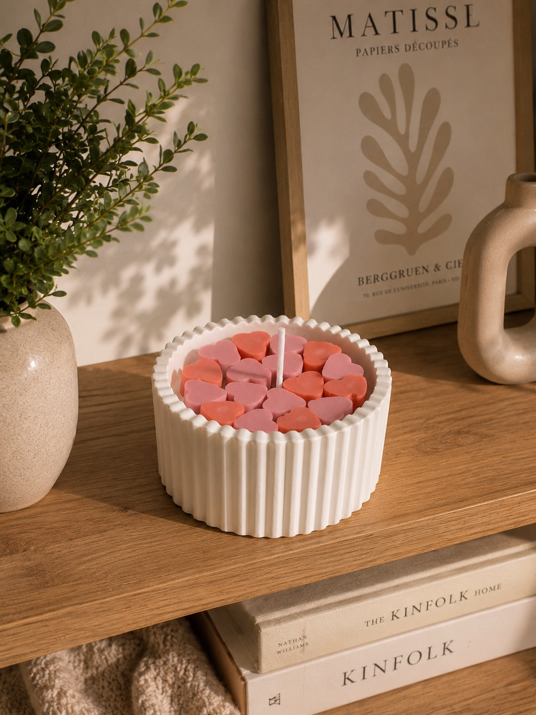 Vela aromática con corazones de cera decorando estantería con libros y cuadro Matisse – Casa Calma