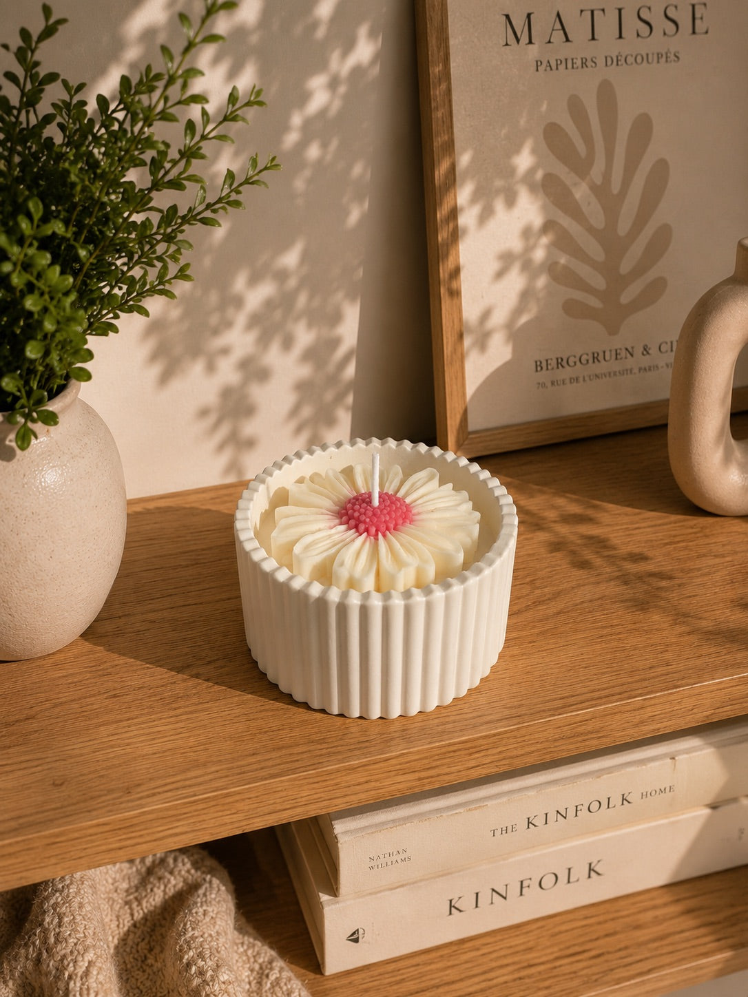 Vela aromática con margarita de cera decorando estantería con libros y cuadro – Casa Calma