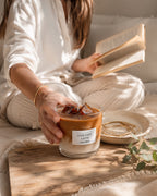 Mujer sosteniendo la vela Iced Café Latte de Casa Calma mientras lee un libro, ambiente acogedor y relajado