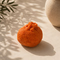 Wax melt artesanal con forma de mandarina elaborado con cera de soja, sobre superficie beige con sombras de hojas – Casa Calma