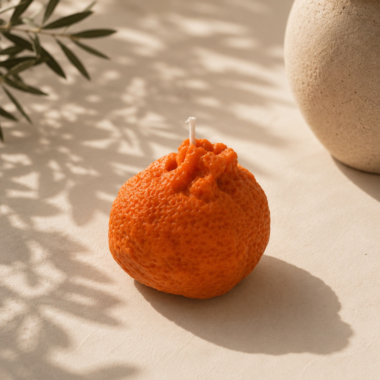 Wax melt artesanal con forma de mandarina elaborado con cera de soja, sobre superficie beige con sombras de hojas – Casa Calma