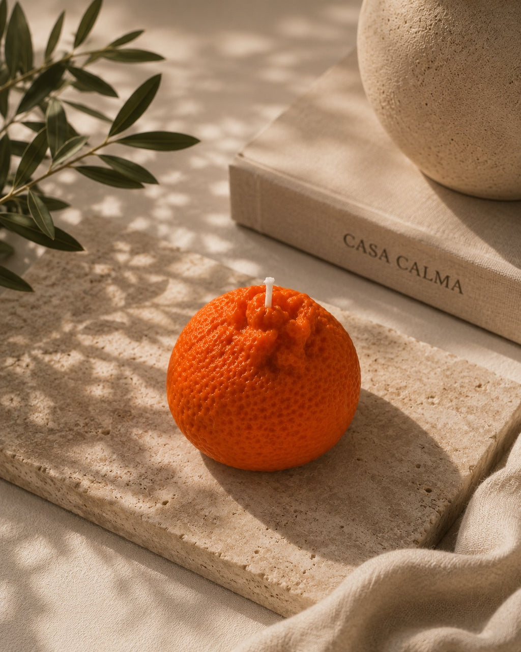 Wax melt Mandarina Artesanal XL sobre tabla de piedra junto al libro de Casa Calma, con luz cálida y hojas de olivo