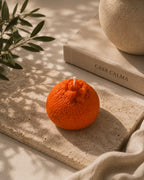 Wax melt Mandarina Artesanal XL sobre tabla de piedra junto al libro de Casa Calma, con luz cálida y hojas de olivo
