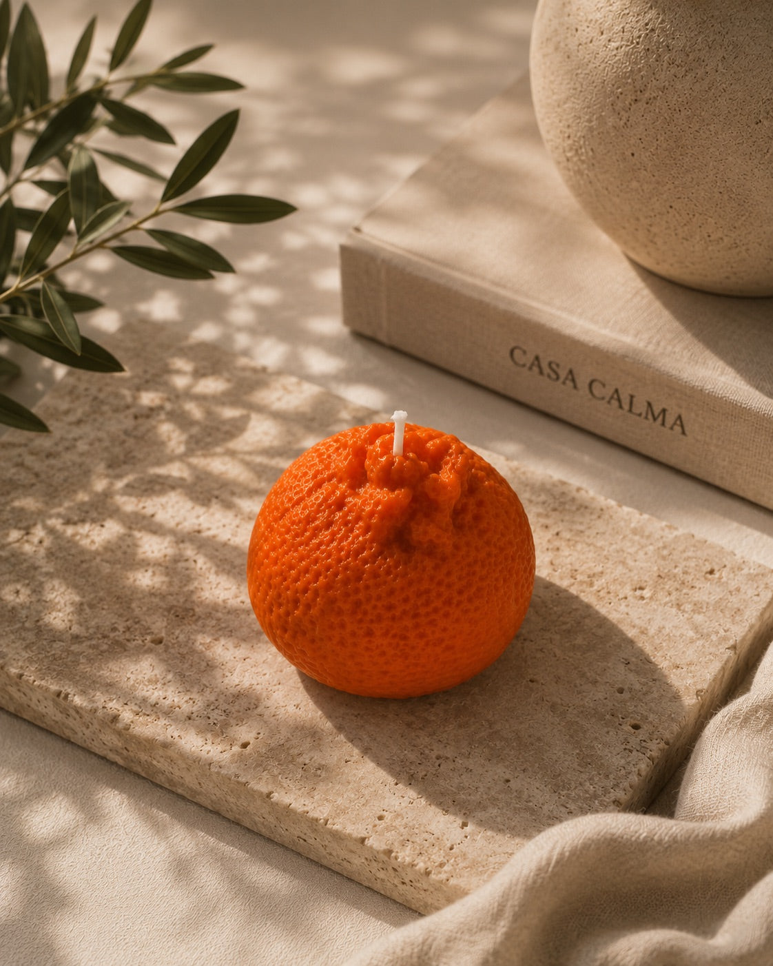 Wax melt Mandarina Artesanal XL sobre tabla de piedra junto al libro de Casa Calma, con luz cálida y hojas de olivo